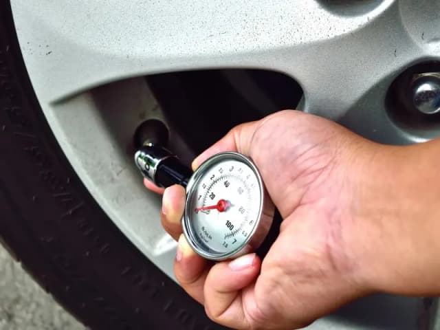 Hand checking tyre pressure with a gauge on the valve